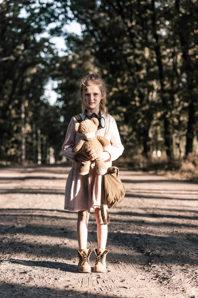 Garoto bonito segurando brinquedo macio sujo perto de árvores em chernobyl, conceito pós-apocalíptico — Fotografia de Stock