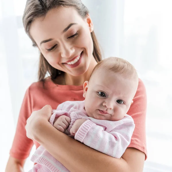 Mère souriante tenant dans les bras adorable petite fille à la maison — Photo de stock