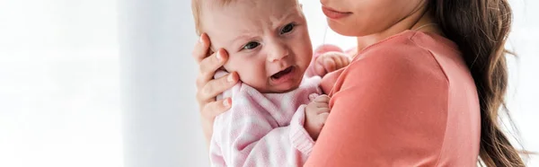 Panoramic shot of mother holding in arms crying infant daughter at home — Stock Photo