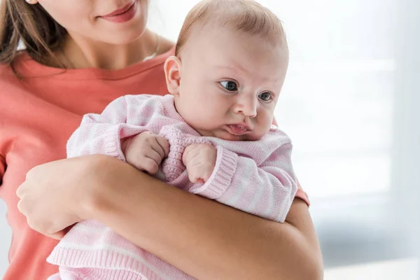 Abgeschnittene Ansicht einer lächelnden Frau, die ihre entzückende kleine Tochter zu Hause im Arm hält — Stockfoto