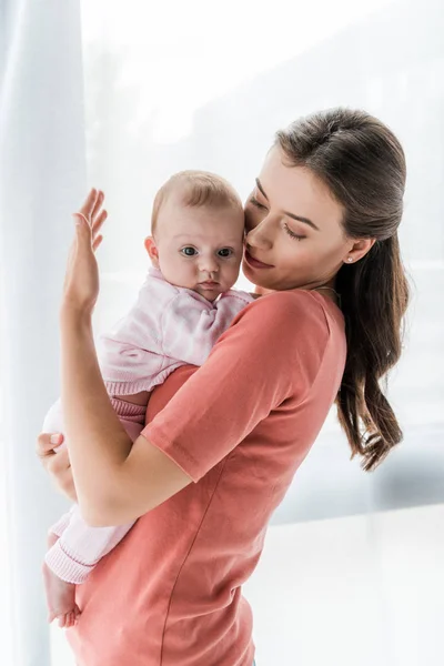 Mãe atraente segurando nos braços bebê filha em casa — Fotografia de Stock