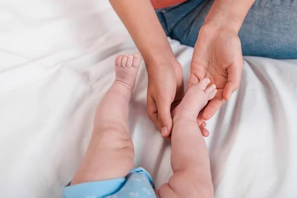 Vista ritagliata della madre che tocca la gamba del bambino mentre fa un massaggio in camera da letto — Foto stock