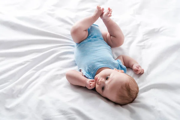 Adorable bébé en bébé barboteuse couché sur le lit à la maison — Photo de stock