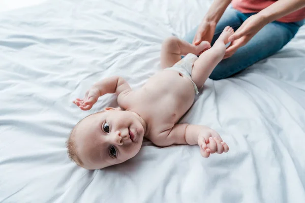 Abgeschnittene Ansicht der Mutter, die Beine des niedlichen Säuglings zu Hause berührt — Stockfoto