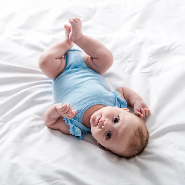 Entzückender Säugling im blauen Babybody zu Hause auf dem Bett liegend — Stockfoto