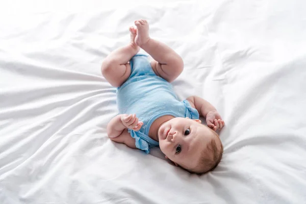 Cute infant in blue baby bodysuit lying on bed at home — Stock Photo