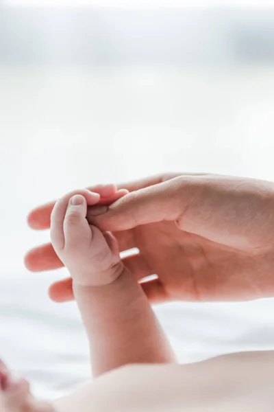 Vista recortada de la mujer haciendo masaje mientras toca la mano del bebé bebé - foto de stock