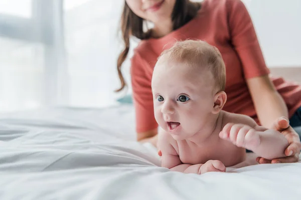 Vista ritagliata di donna felice toccare figlia bambino sdraiato sul letto a casa — Foto stock