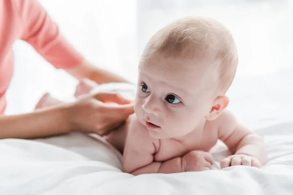 Cropped view of mother doing massage to baby daughter lying on bed at home — Stock Photo