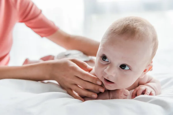 Recortado vista de la madre haciendo masaje a lindo bebé hija acostado en la cama en casa - foto de stock