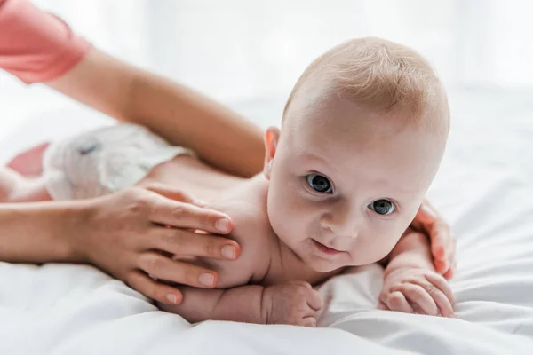 Cropped view of mother doing massage to cute infant daughter lying on bed at home — Stock Photo