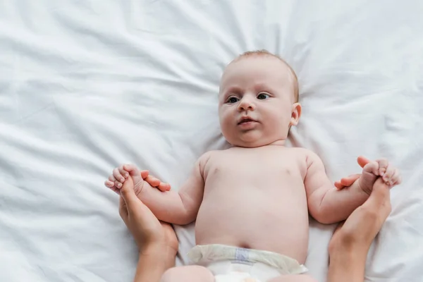 Visão recortada da mãe segurando as mãos da adorável filha bebê na fralda — Fotografia de Stock