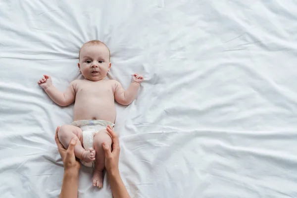 Visão recortada da mãe tocando as pernas da filha bebê na fralda — Fotografia de Stock