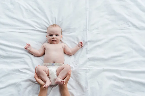 Vista cortada da mãe tocando pernas de adorável bebê filha na fralda — Fotografia de Stock