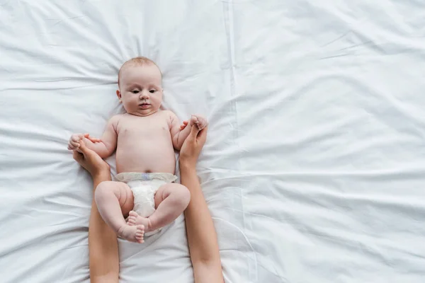 Vista recortada de la madre cogida de la mano de la adorable hija bebé con los pies descalzos - foto de stock