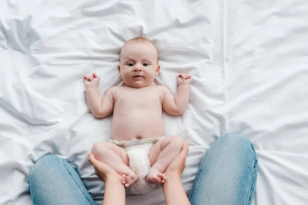 Vue recadrée de la mère en jeans touchant adorable bébé fille avec pieds nus — Photo de stock