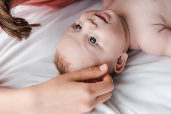 Обрезанный вид заботливой матери, трогающей милого младенца на кровати — стоковое фото