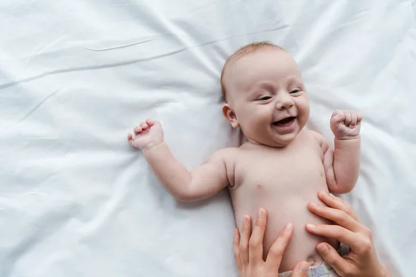 Вид сверху на мать, трогающую положительную младенческую дочь на кровати — стоковое фото