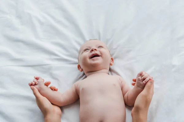 Vue du dessus de la mère tenant les mains de la fille bébé souriante sur le lit — Photo de stock