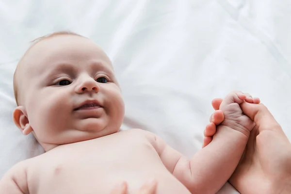 Обрезанный вид матери, держащей за руку симпатичную младенческую дочь на кровати — стоковое фото