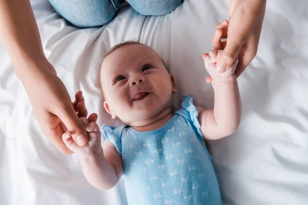 Abgeschnittene Ansicht der Mutter, die die Hände eines entzückenden Säuglings hält, der die Zunge herausstreckt — Stockfoto