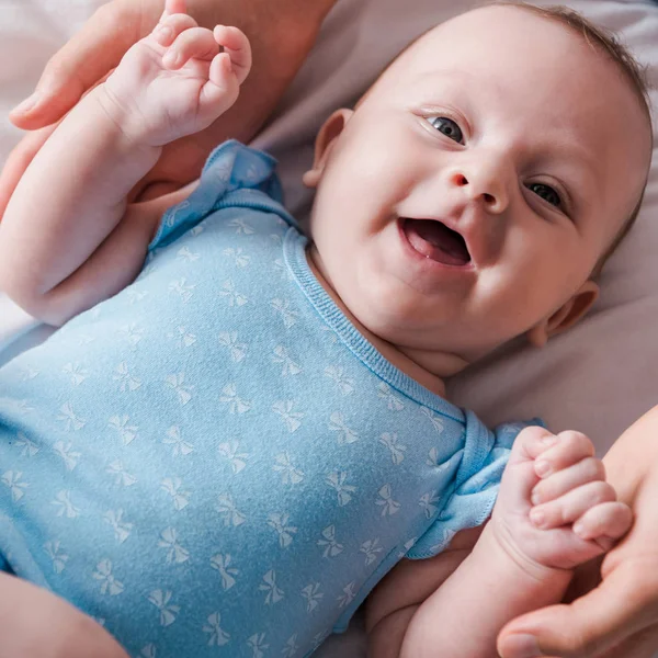 Обрезанный вид матери, держащейся за руки счастливого младенца в синем купальнике — стоковое фото