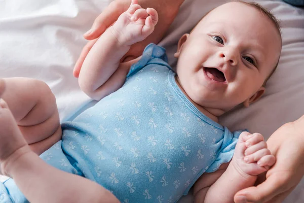 Cropped view of woman holding hands of happy infant in blue baby bodysuit — Stock Photo