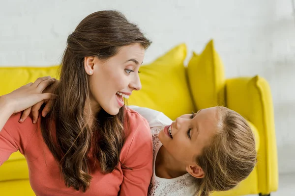 Niño feliz sonriendo mientras mira niñera alegre en la sala de estar - foto de stock