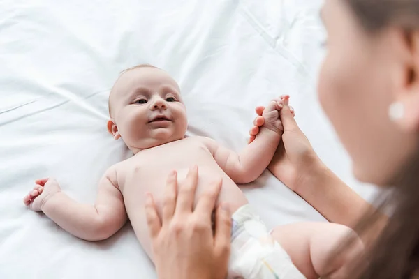 Selective focus of caring mother touching cute infant daughter on bed — Stock Photo