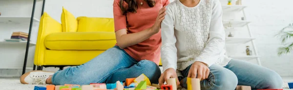 Panoramic shot of babysitter and kid near toy blocks in living room — Stock Photo