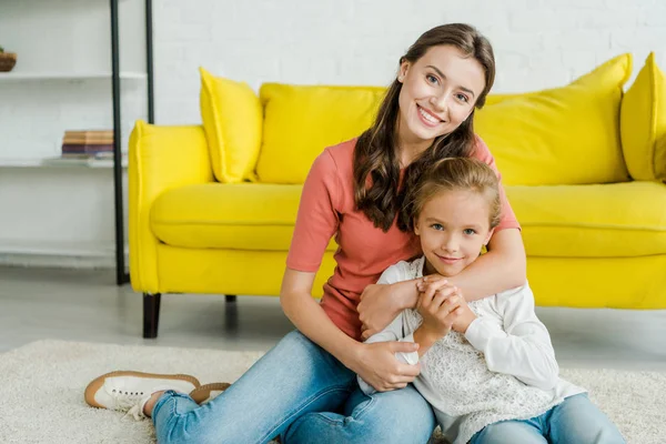 Niñera atractiva abrazando niño feliz en la sala de estar - foto de stock