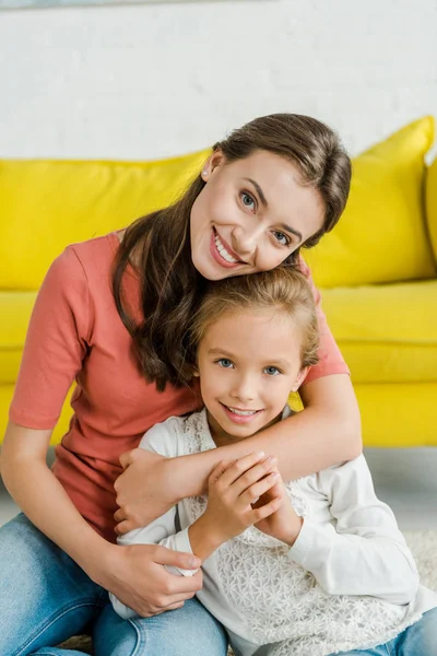 Attractive babysitter hugging cheerful kid in living room — Stock Photo