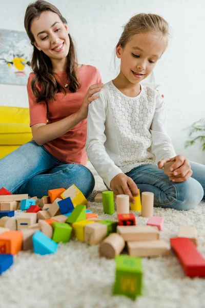 Foco seletivo de criança brincando com blocos de brinquedo perto de babá alegre — Fotografia de Stock