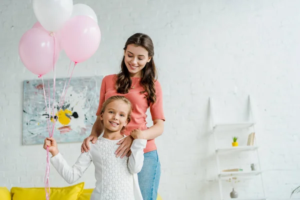 Niño feliz sosteniendo globos rosados cerca de niñera alegre - foto de stock