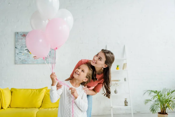 Niñera alegre mirando globos rosados cerca de niño feliz - foto de stock