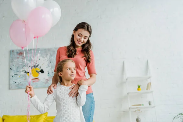 Feliz niñera de pie con hija sosteniendo globos rosados - foto de stock