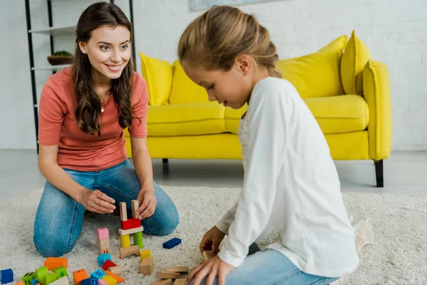 Selective focus of babysitter looking at kid near toy blocks on carpet — Stock Photo