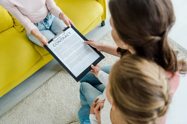 Overhead view of mother standing with daughter and giving clipboard to babysitter — Stock Photo