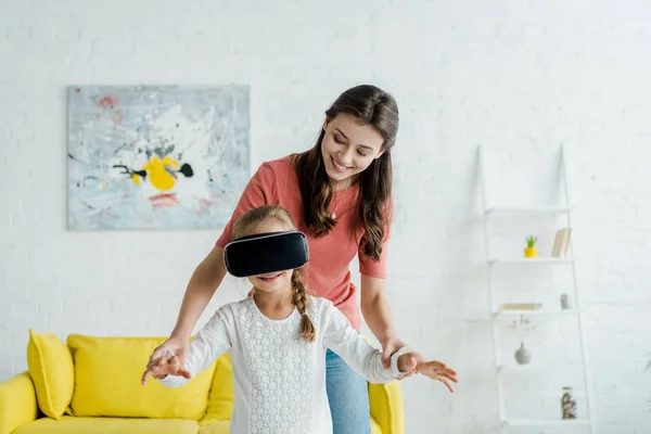 Happy babysitter looking at cute kid in virtual reality headset — Stock Photo