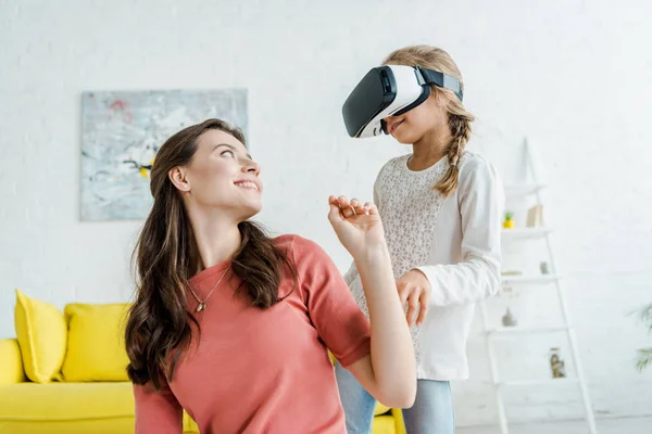 Niñera feliz mirando niño alegre en auriculares de realidad virtual - foto de stock