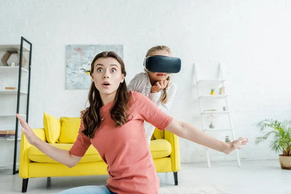 Surprised babysitter with outstretched hands near kid in virtual reality headset — Stock Photo