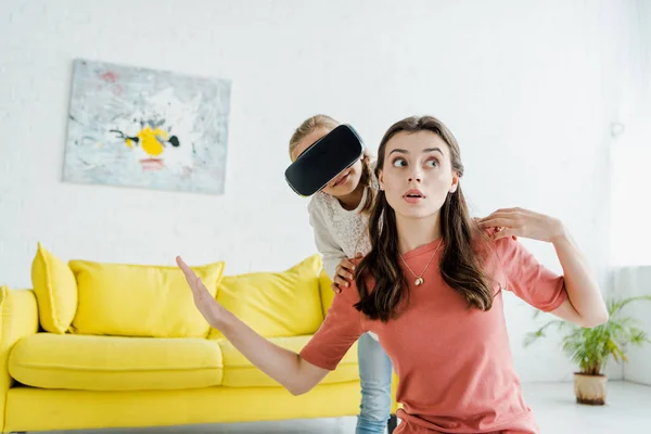 Surprised babysitter with outstretched hands near child in virtual reality headset — Stock Photo