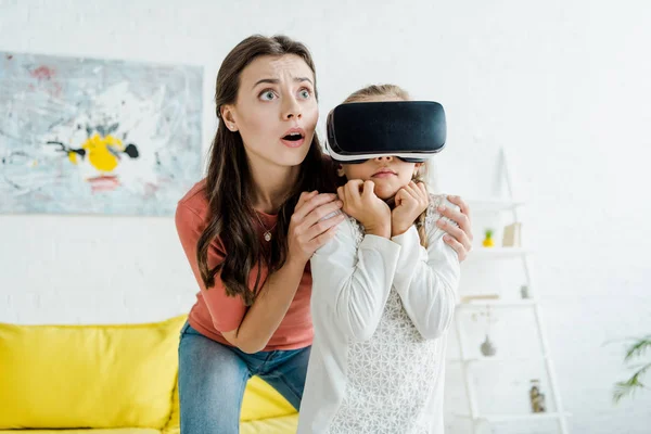 Babá chocado de pé perto criança assustada em fone de ouvido realidade virtual — Fotografia de Stock
