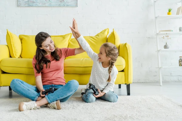 KYIV, UKRAINE - SEPTEMBER 4, 2019: babysitter giving high five to happy kid holding joystick in living room — Stock Photo