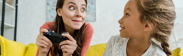 KYIV, UKRAINE - SEPTEMBER 4, 2019: panoramic shot of babysitter looking at happy kid while holding joystick in living room — Stock Photo