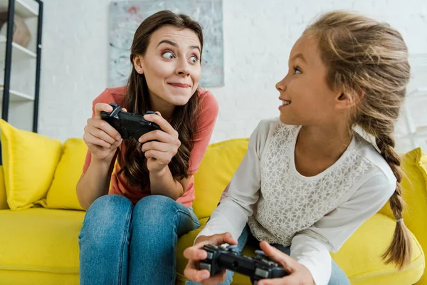 KYIV, UCRANIA - 4 de septiembre de 2019: niñera mirando a un niño feliz sosteniendo el joystick en la sala de estar - foto de stock