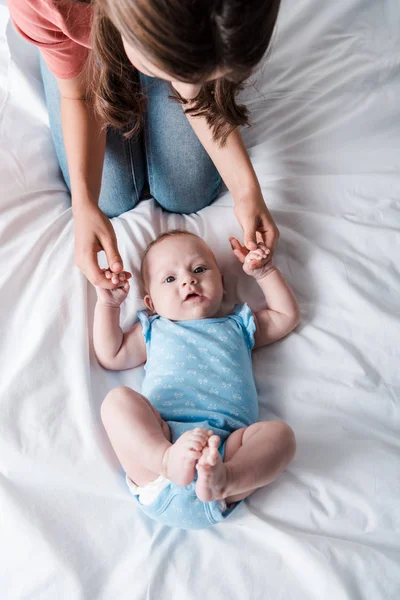 Вид зверху на матір в джинсах, що сидять біля чарівного немовляти в синьому костюмі для немовлят — стокове фото