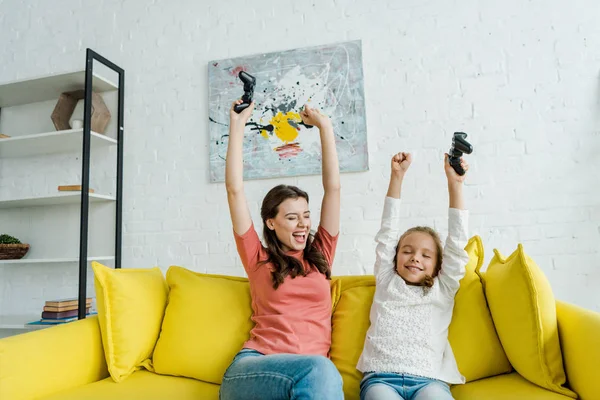 KYIV, UCRANIA - 4 de septiembre de 2019: niñera alegre y niño feliz celebrando el triunfo mientras sostiene joysticks en el salón - foto de stock