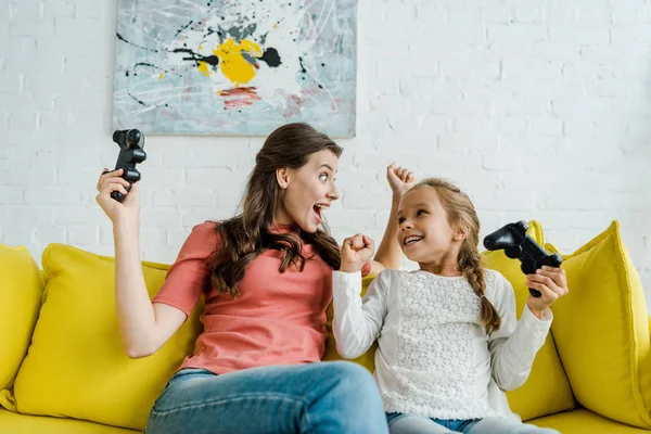 KYIV, UCRAINA - 4 SETTEMBRE 2019: babysitter entusiasta e bambino felice festeggiano il trionfo tenendo i joystick in salotto — Foto stock
