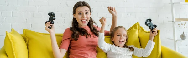 KYIV, UKRAINE - SEPTEMBER 4, 2019: panoramic shot of excited babysitter and happy kid celebrating triumph while holding joysticks in living room — Stock Photo